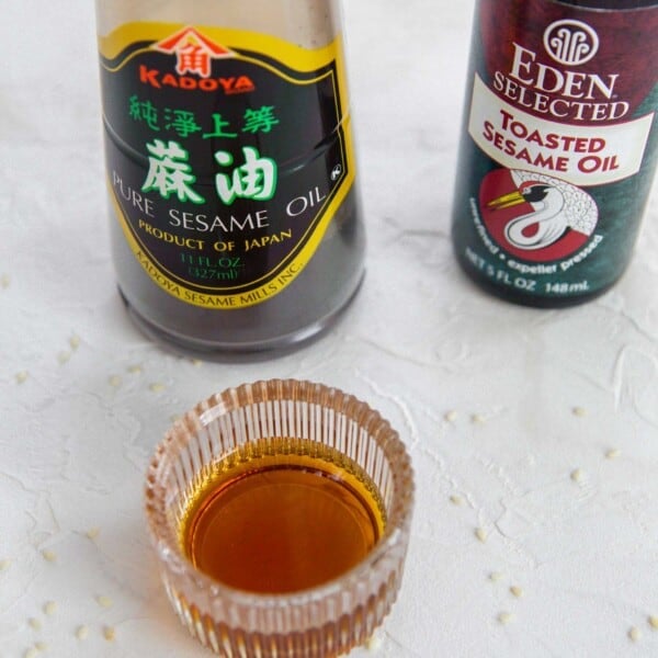 Sesame oil in a glass container with two bottles of sesame oil; one pure and one toasted.