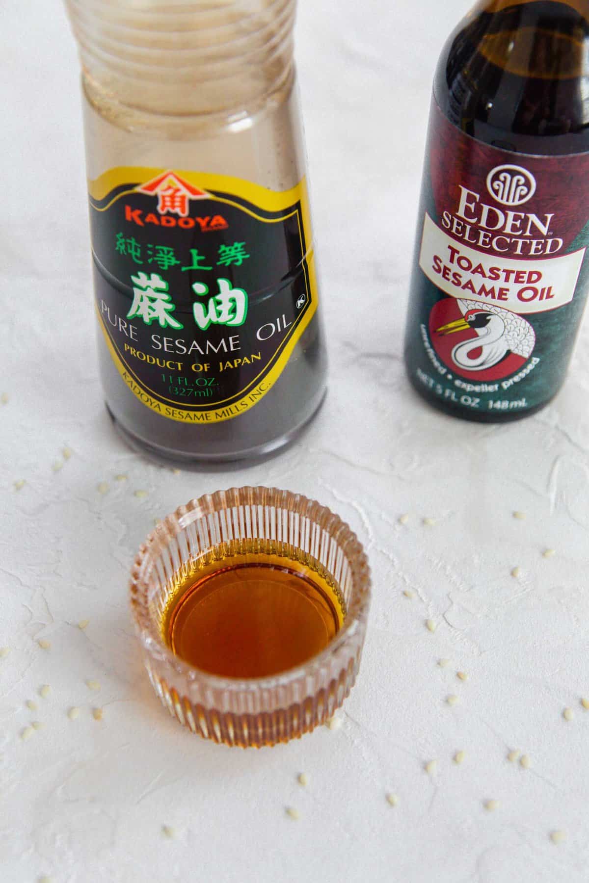Sesame oil in a glass container with two bottles of sesame oil; one pure and one toasted.