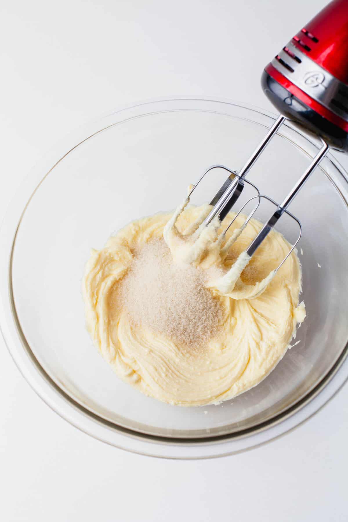 butter and sugar in a large clear bowl being creamed together with a red hand mixer