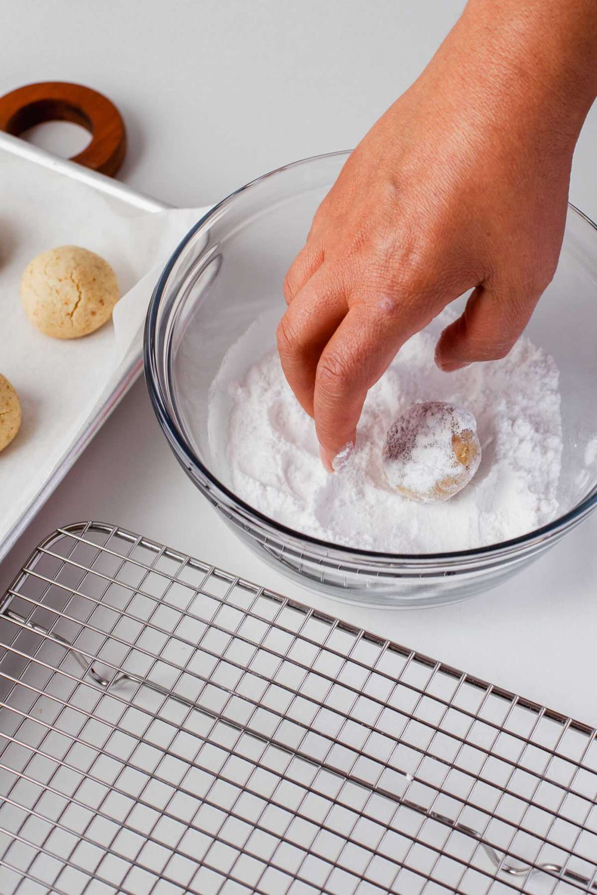 a hand in a bowl of powdered sugar rolling the cookie in it