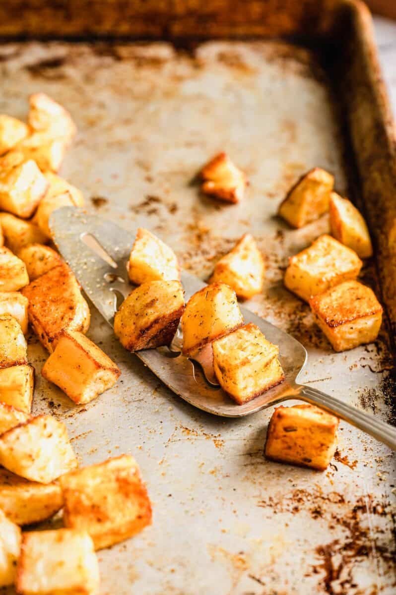 roasted cubed potatoes on a serving spoon on a metal baking sheet