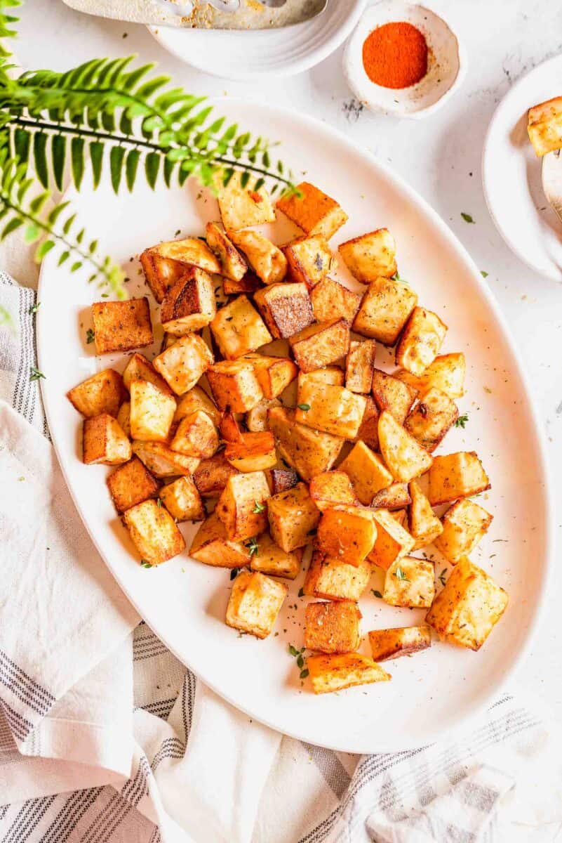 overhead image of roasted potatoes on a large white platter next to a fern