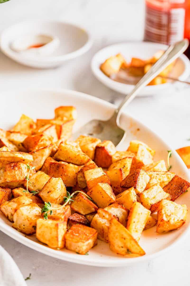 roasted potatoes on a large white platter with a serving spoon on the platter. the roasted potatoes are garnished with fresh thyme
