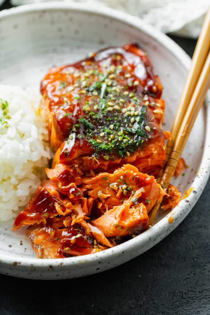 teriyaki glazed salmon filet broken into large pieces on a speckled ceramic plate with wooden chopsticks next to it