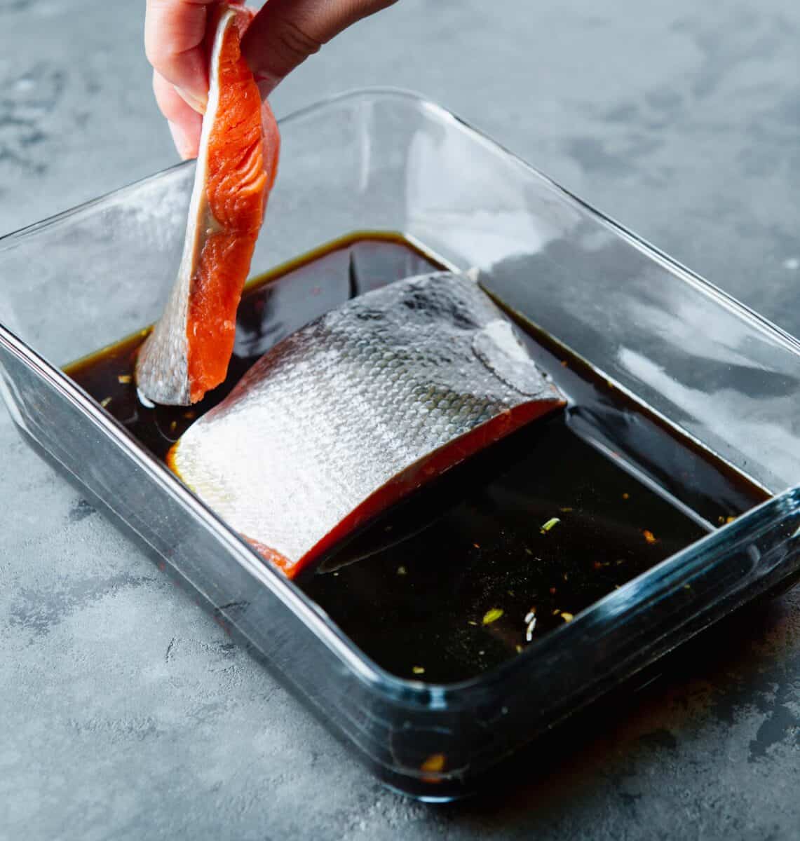 placing salmon flesh side down into the marinade in the glass container