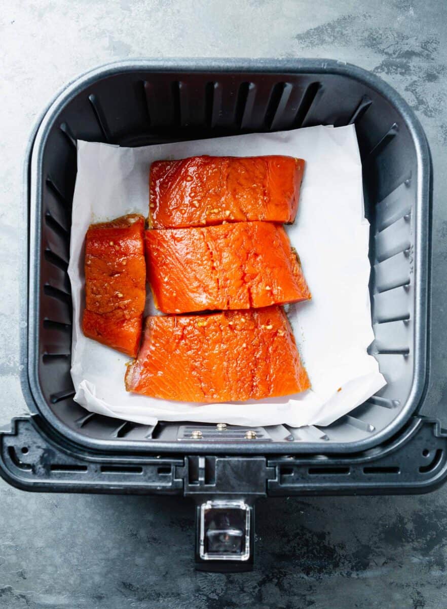 marinated salmon filets on top of parchment paper in the air fryer basket
