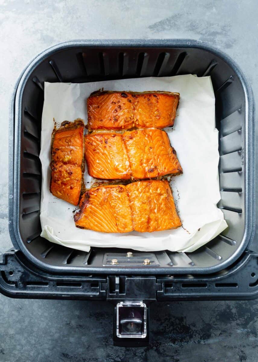 cooked salmon filets in the air fryer basket on top of parchment paper