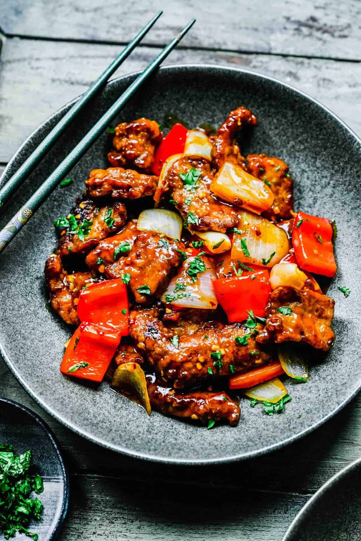 Beijing beef on a plate with chopsticks.