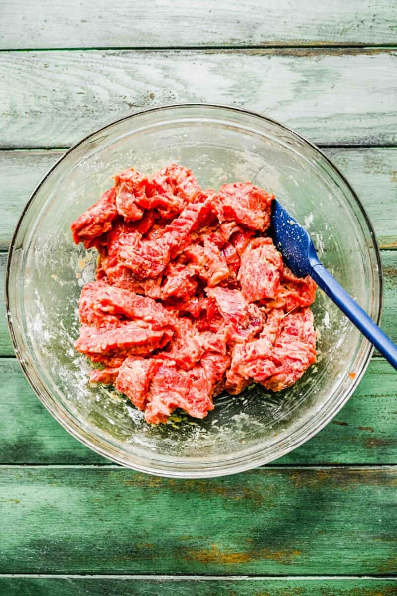 Beef coated in cornstarch in a bowl with a spatula.