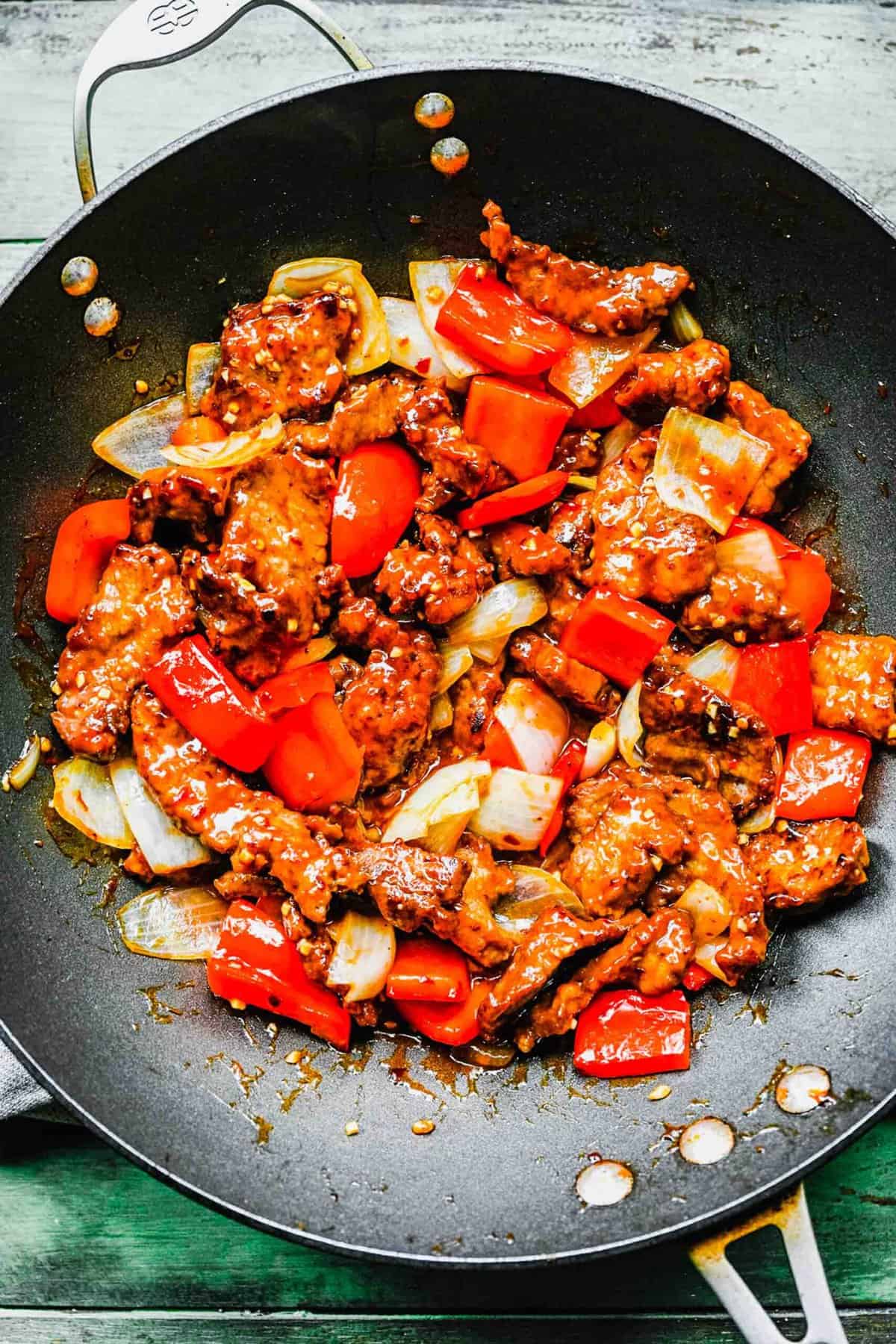 Beijing beef with bell peppers and onions in a wok.