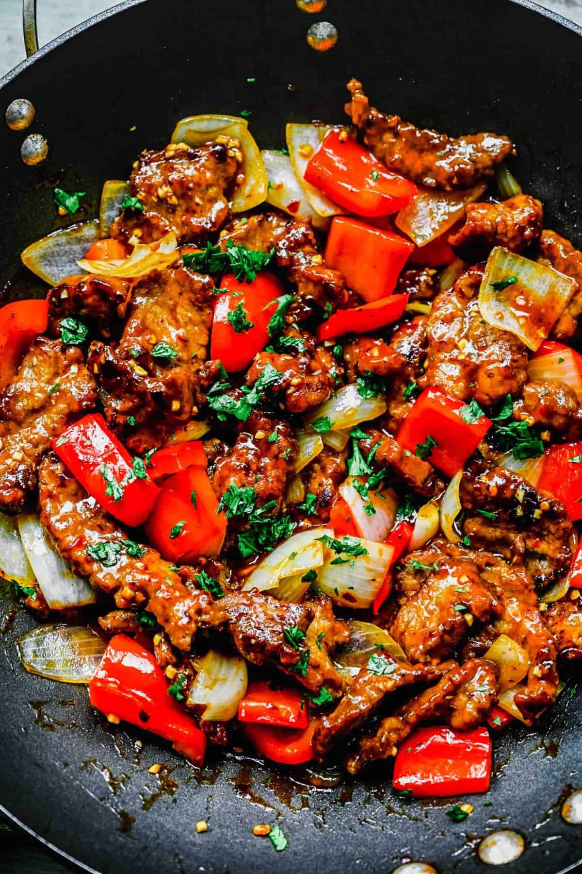 Beijing beef with bell peppers and onions in a wok.