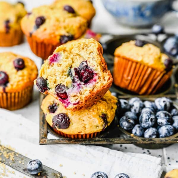 A banana blueberry muffins sliced in half next to whole muffins, a knife, and fresh blueberries.