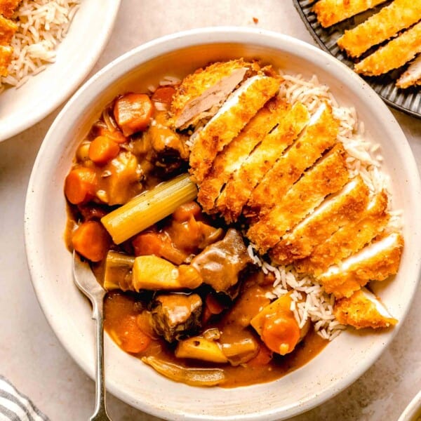 Katsu chicken curry served in a bowl over rice with a fork near a plate of chicken katsu.