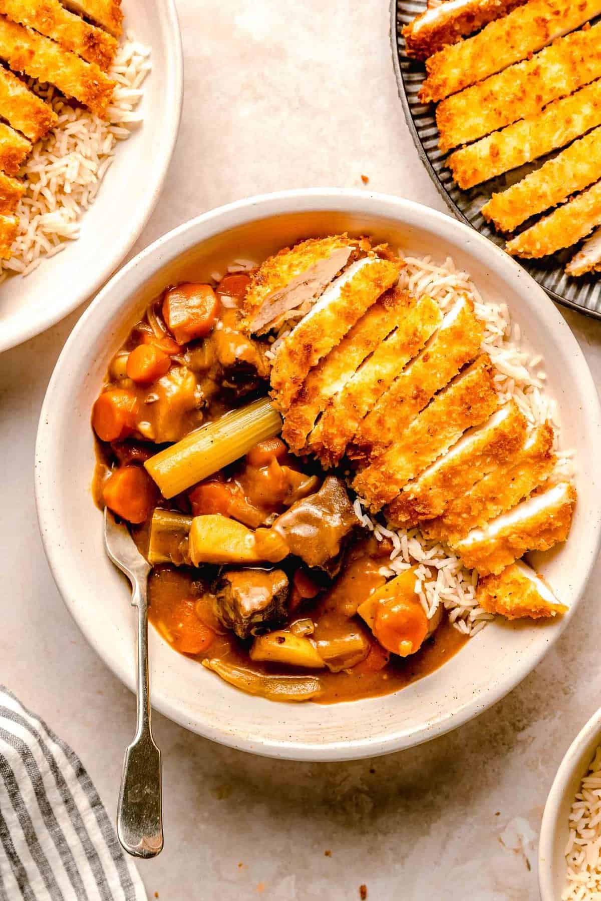 Katsu chicken curry served in a bowl over rice with a fork near a plate of chicken katsu.