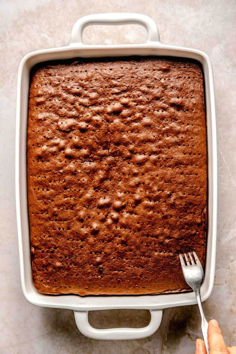 Poking holes with a fork in chocolate tres leches cake.