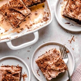 Sliced chocolate tres leches cake on plates with a fork next to a baking dish full of chocolate tres leches cake.