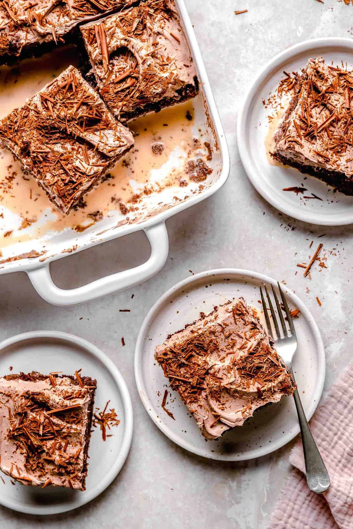 Sliced chocolate tres leches cake on plates with a fork next to a baking dish full of chocolate tres leches cake.