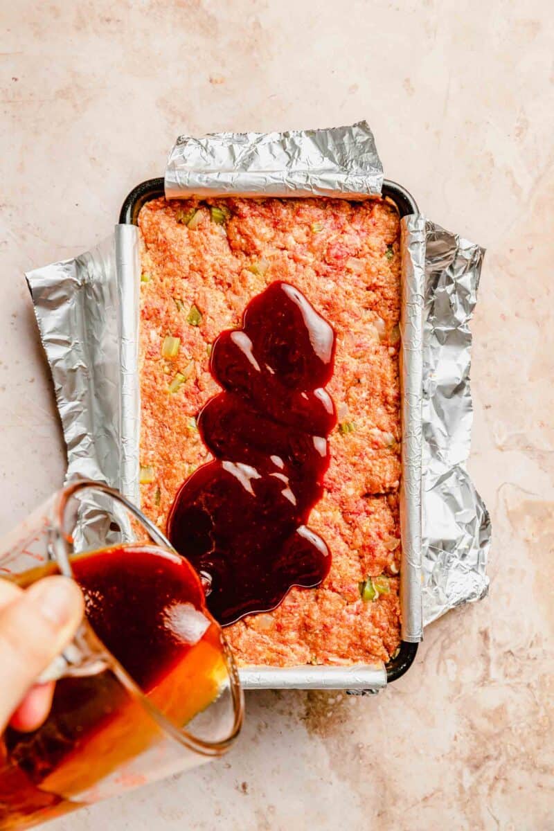 Pouring glaze on classic meatloaf before baking in a loaf pan.