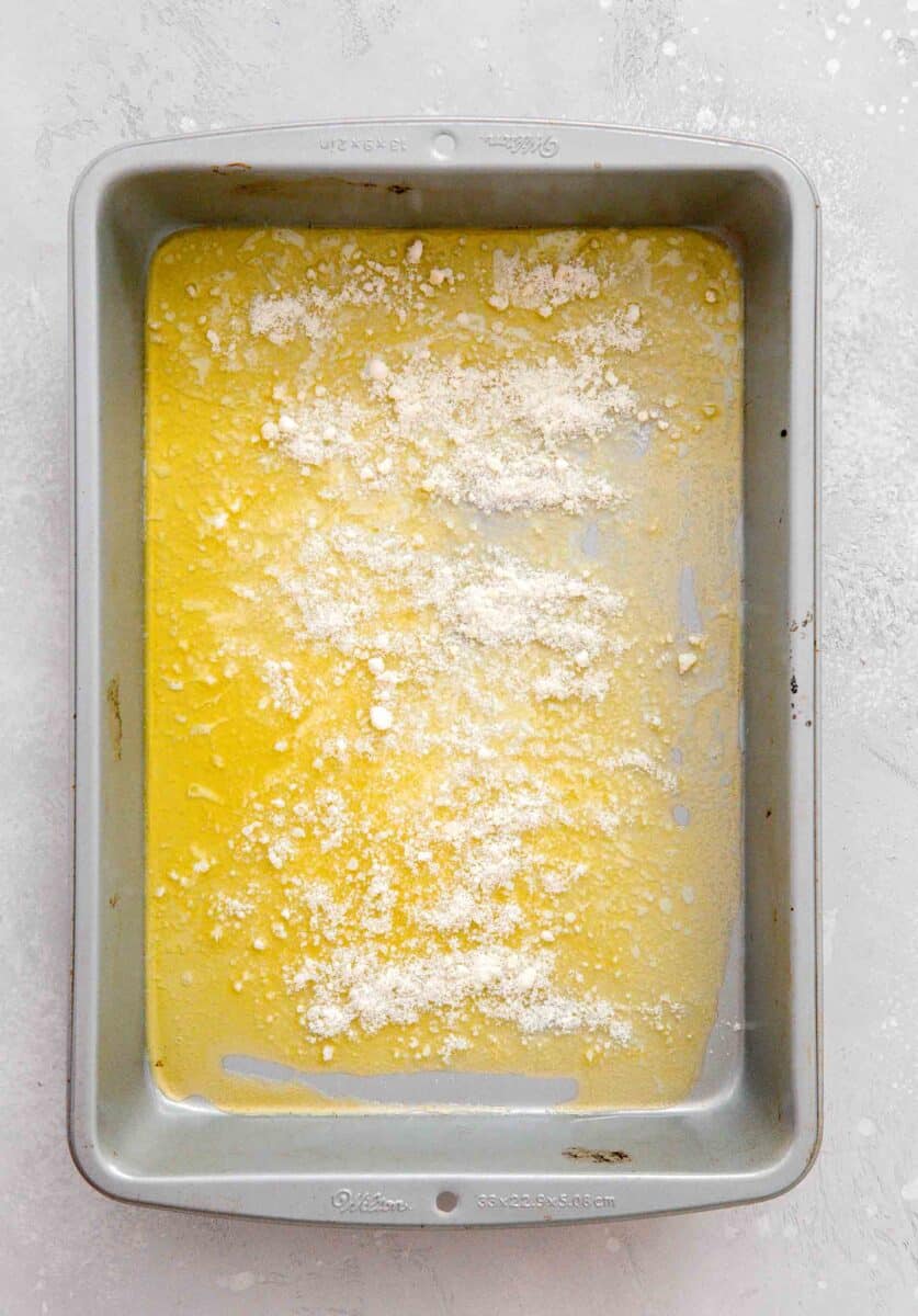 grated parmesan cheese sprinkled on top of the melted butter in the light metal 9x13" baking pan