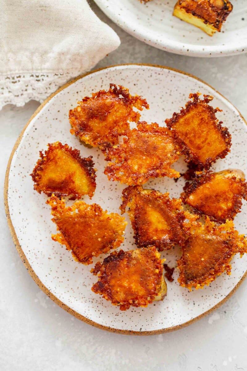 overhead image of browned and crispy parmesan edged potatoes on a speckled ceramic plate next to a linen towel