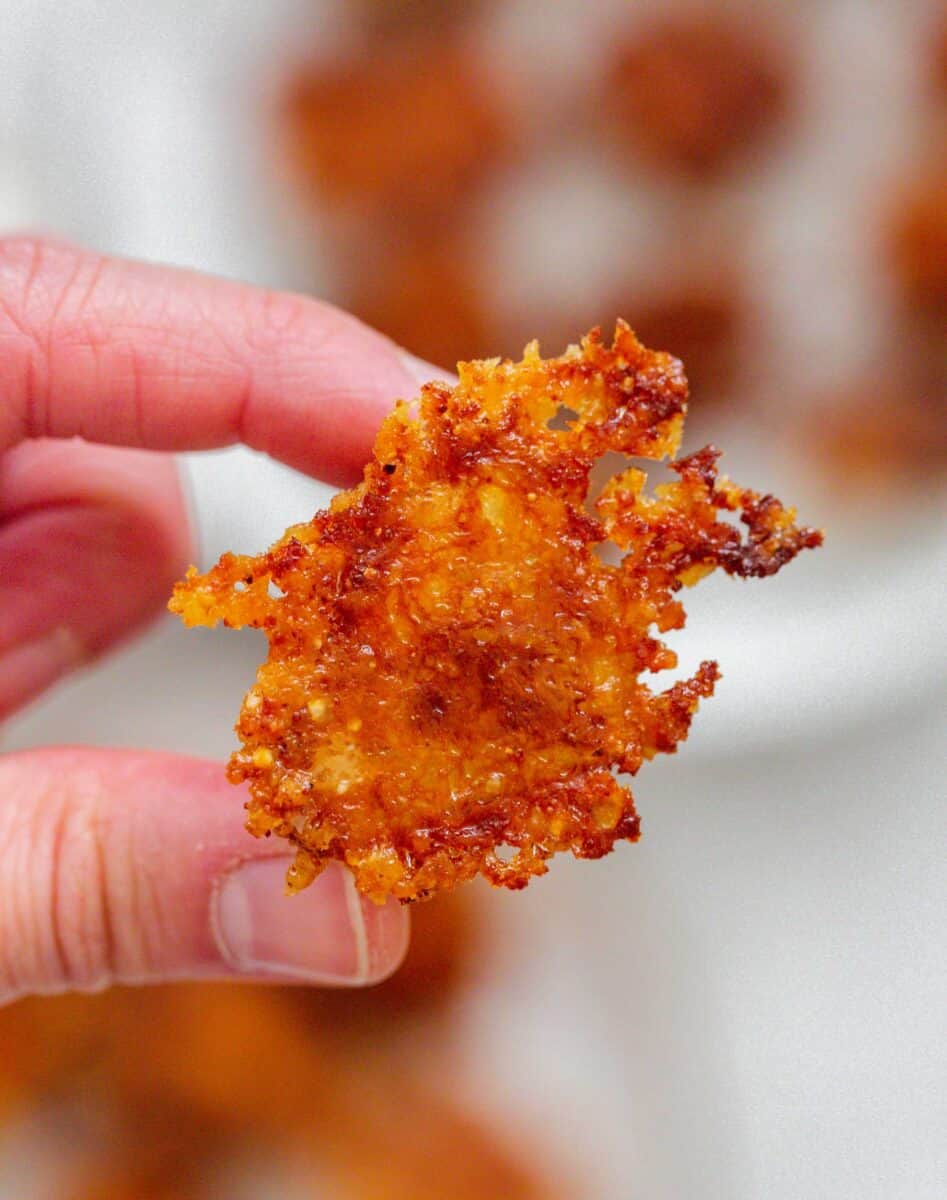a thumb and index finger is holding up a crispy parmesan potato to show the crispy edge