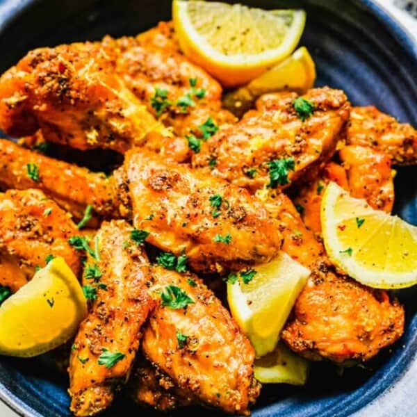 Lemon pepper chicken wings on a platter with lemon wedges.