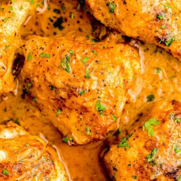 up close image of smothered chicken thigh on a bed of gravy next to other pieces of browned chicken