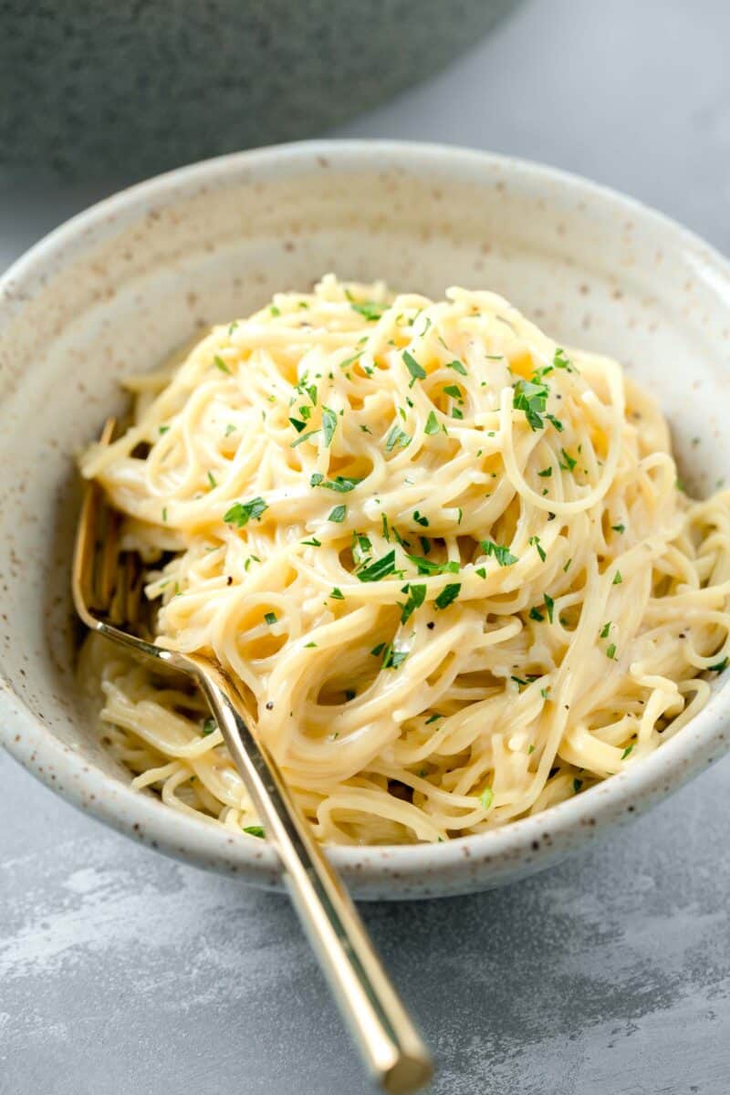 garlic parmesan pasta in a speckled beige ceramic bowl with a gold folk