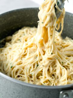 tongs holding a large amount of garlic parmesan pasta in a nonstick skillet