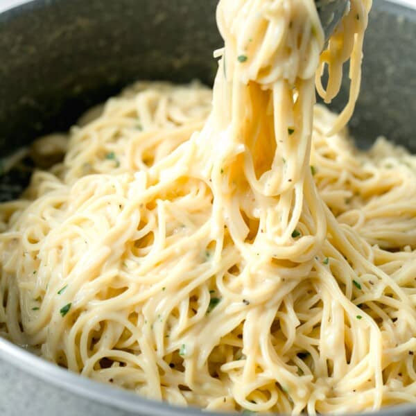 tongs holding a large amount of garlic parmesan pasta in a nonstick skillet