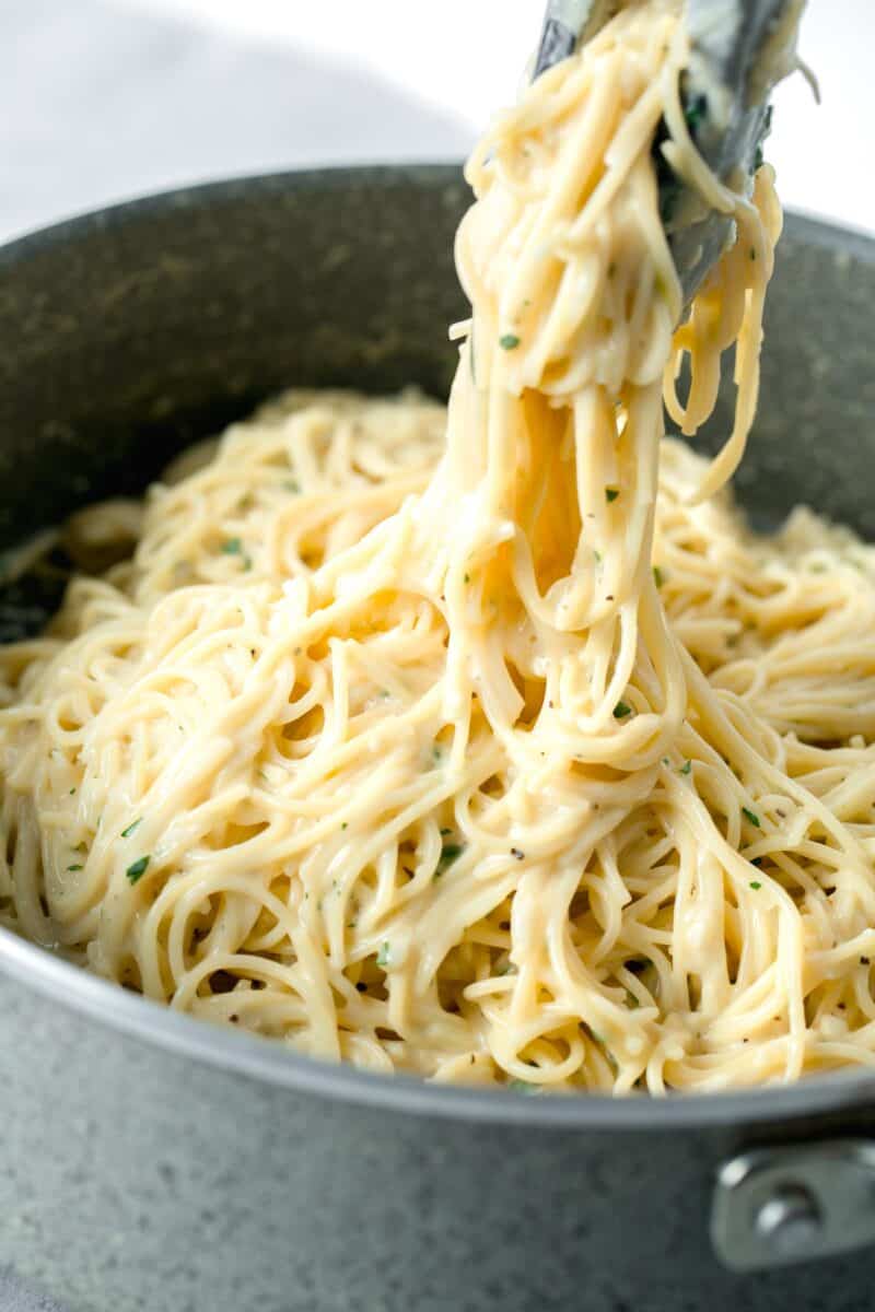 tongs holding a large amount of garlic parmesan pasta in a nonstick skillet