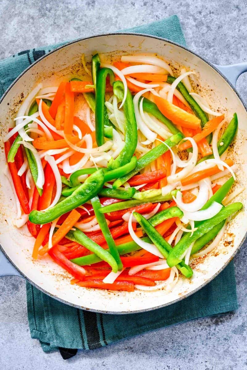 adding bell peppers and sliced onions into cast iron skillet