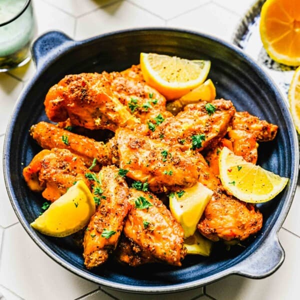 Lemon pepper chicken wings on a platter with lemon wedges near 2 drinking glasses.