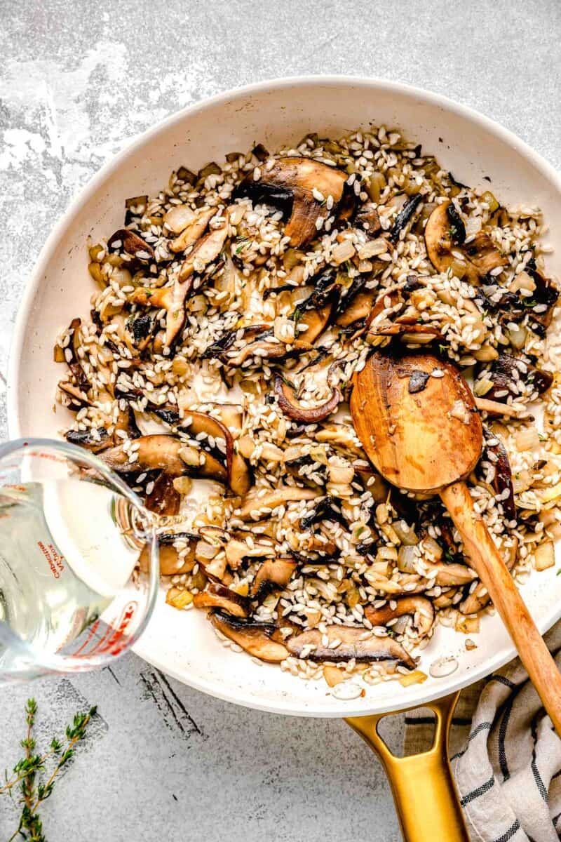 Adding white wine to mushroom risotto with a wooden spoon.