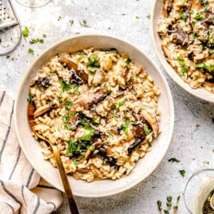 Mushroom risotto in dinner bowls with a spoon next to a glass of white wine and garnished with fresh parsley.