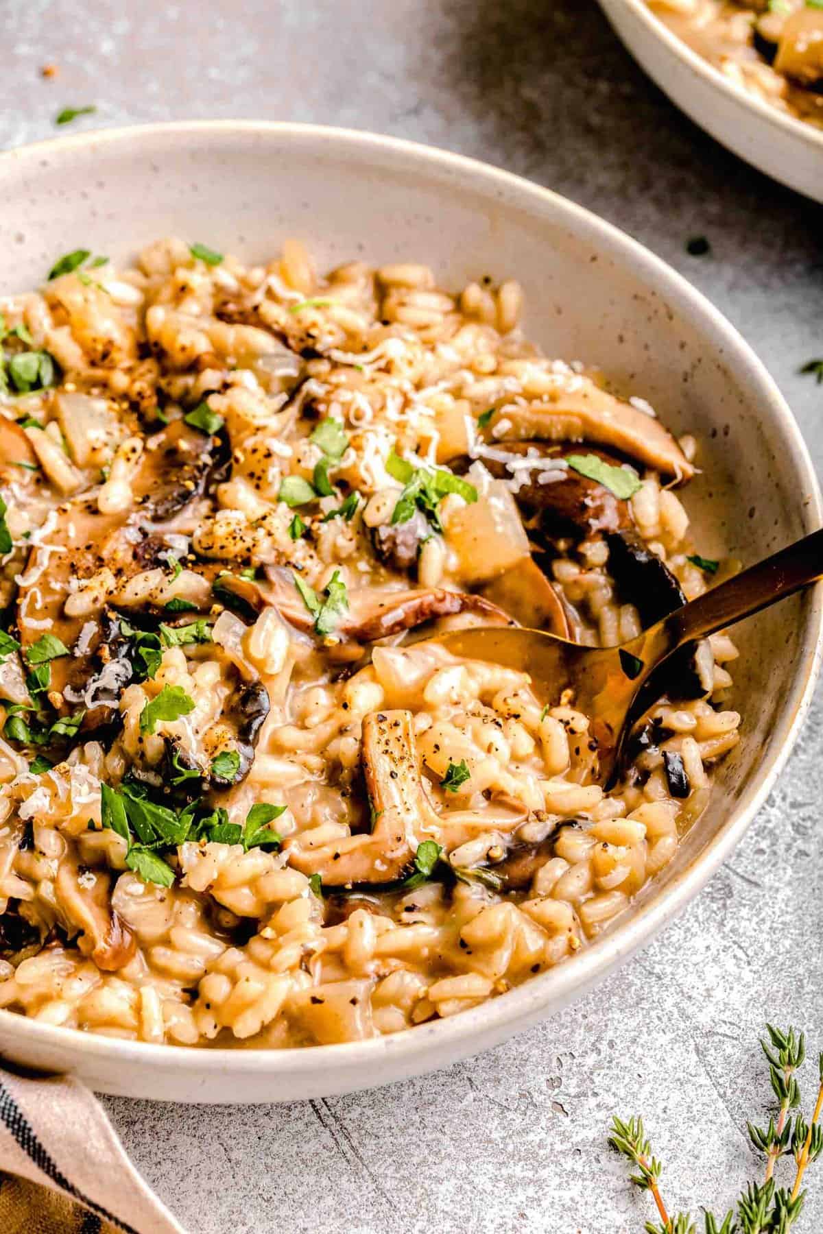 Mushroom risotto in a dinner bowl with a spoon; garnished with fresh parsley.