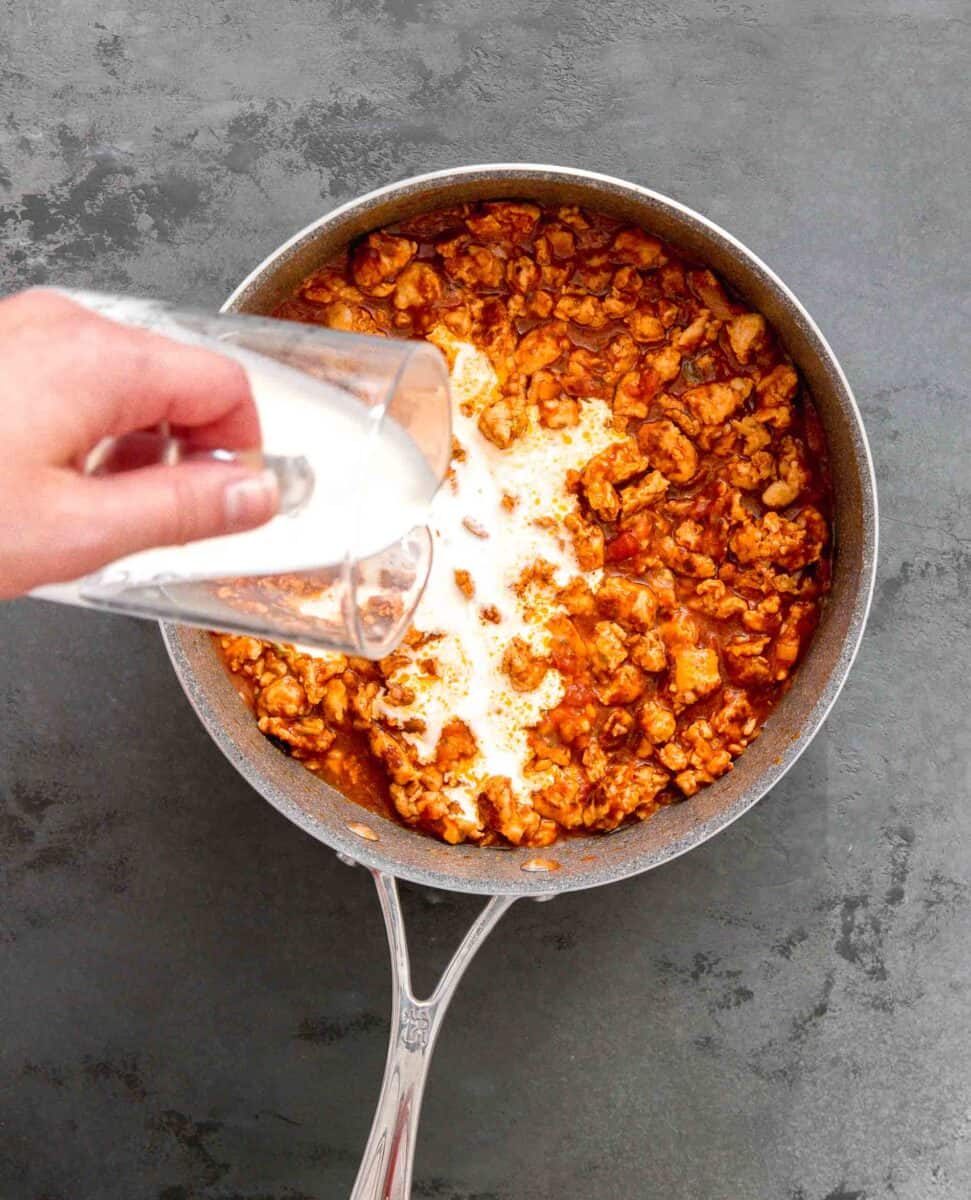 heavy cream being poured onto chicken sausage mixture in the skillet