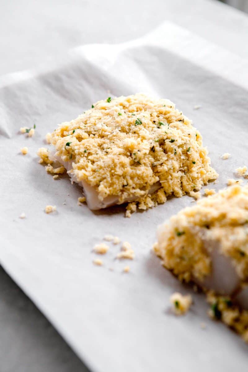 panko parmesan crust on top of a filet of cod that is sitting on a parchment paper lined baking sheet