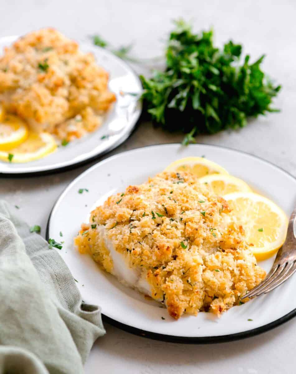 panko parmesan cod on a plate with lemon slices next to a bunch of fresh parsley and green linen towel