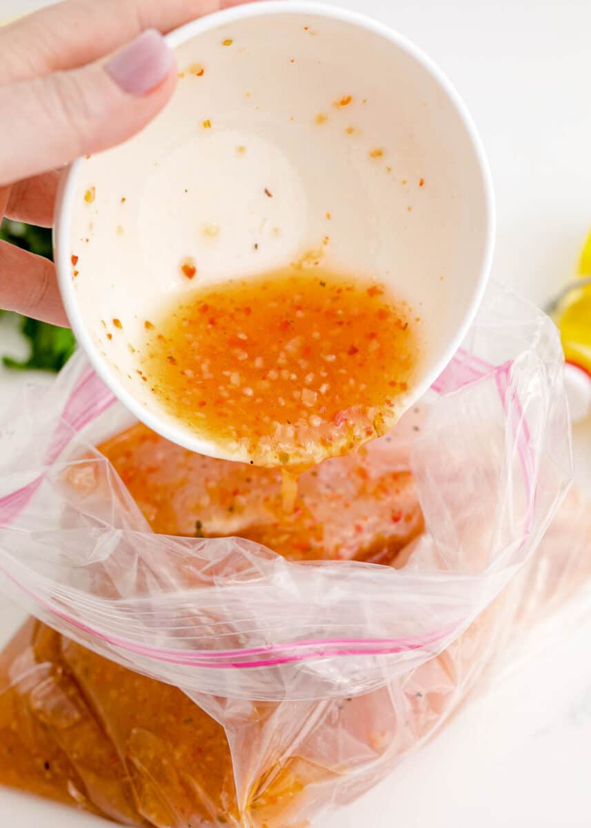 pouring italian dressing in a plastic bag with chicken