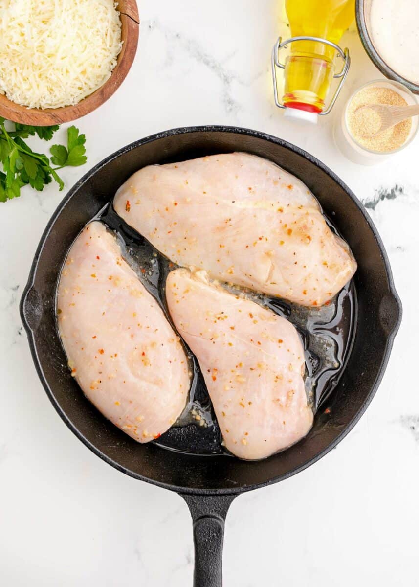marinated chicken breasts being pan-fried in a cast iron skillet