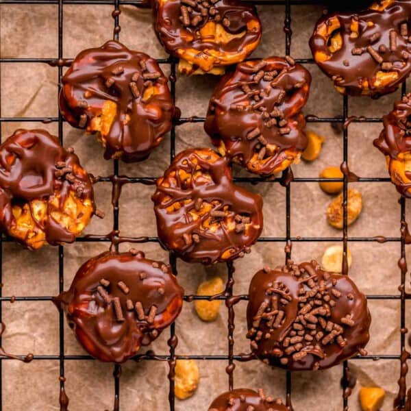 peanut butter pretzel bites half covered in chocolate with chocolate sprinkles on a metal baking sheet