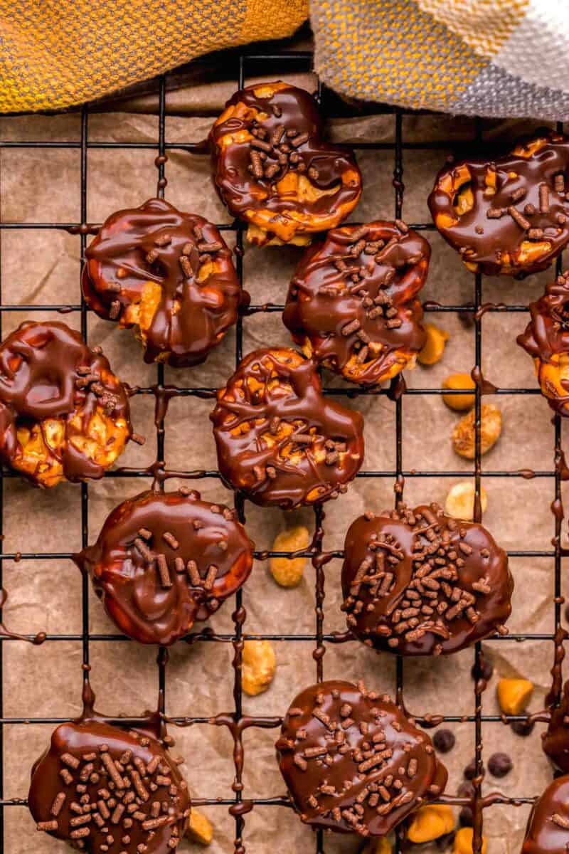 peanut butter pretzel bites half covered in chocolate with chocolate sprinkles on a metal baking sheet