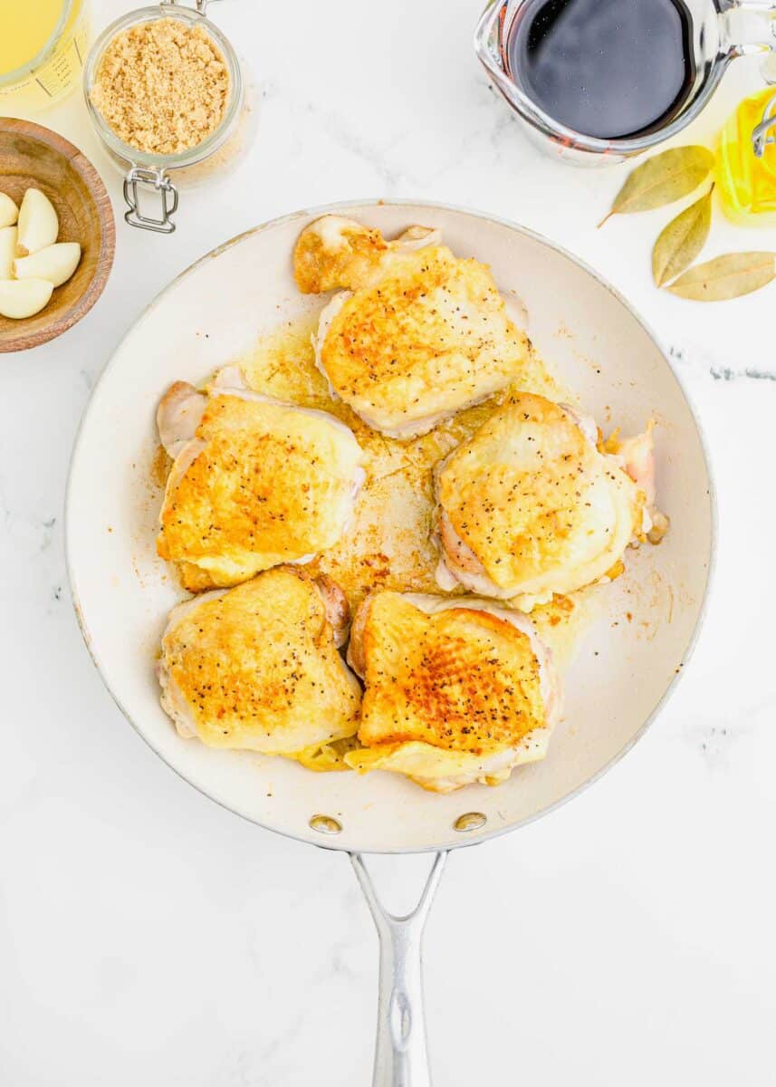 browned and seared bone-in, skin-on chicken thighs in a white nonstick skillet