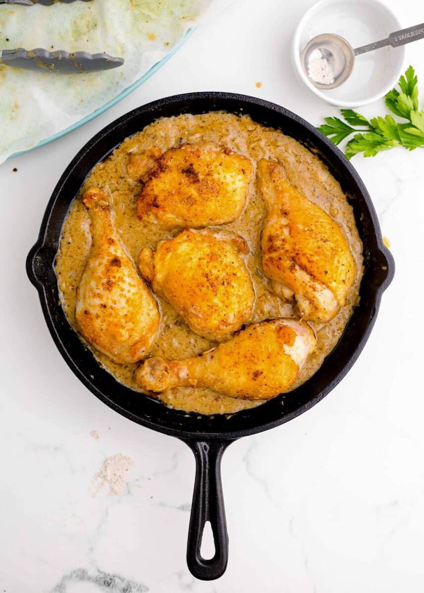 browned chicken being nestled on top of the gravy in the cast iron skillet