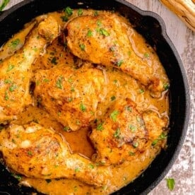 smothered chicken in a cast iron skillet with fresh parsley sprinkled on top and next to the cast iron skillet