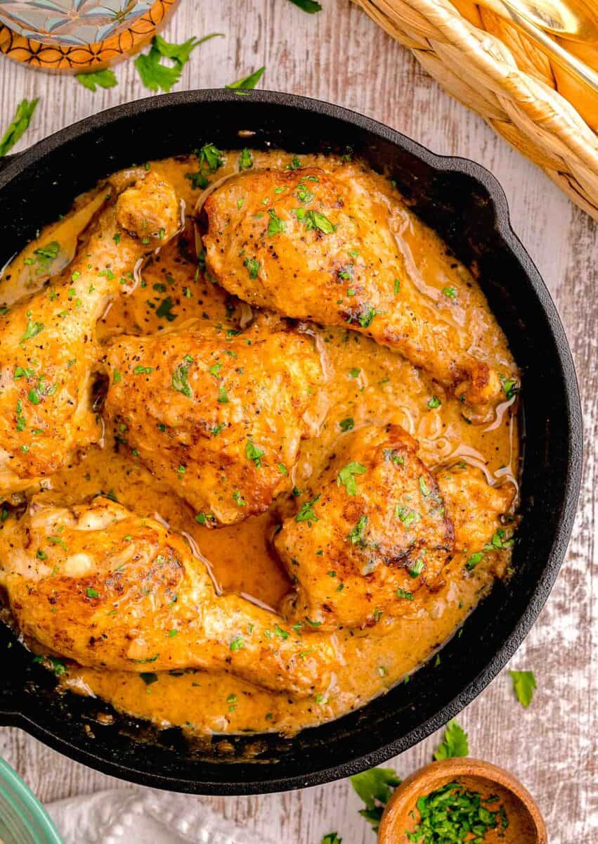 smothered chicken in a cast iron skillet with fresh parsley sprinkled on top and next to the cast iron skillet