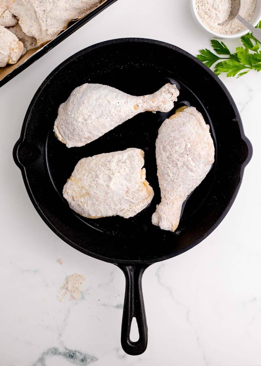 pan-frying floured chicken legs and thighs in a cast iron skillet