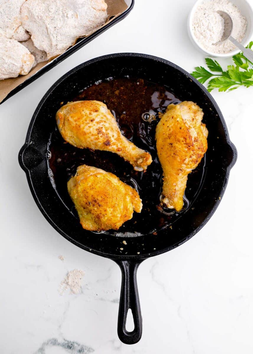 browned chicken legs and thighs in a cast iron skillet
