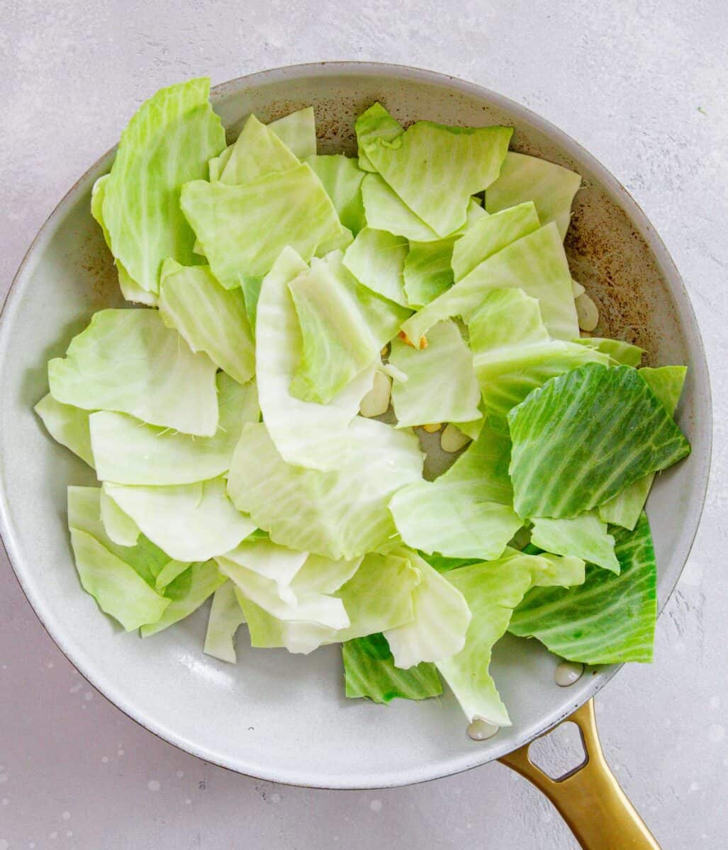 hand torn cabbage in a skillet with garlic slices